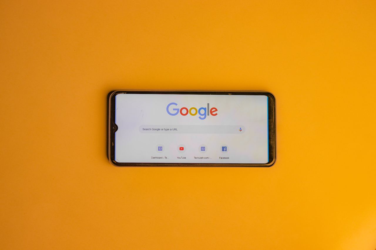 about-us Smartphone displaying Google search page on a vibrant yellow background.